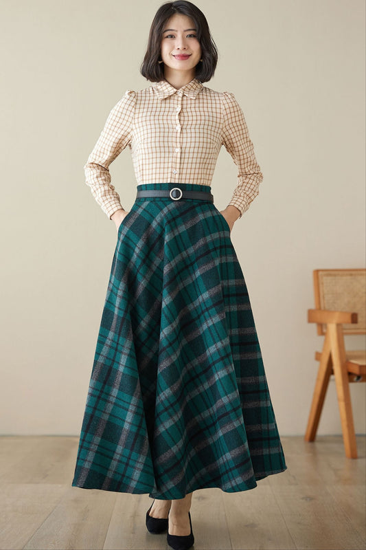 A woman wearing a long wool plaid skirt with a flared design, paired with a checkered shirt and a belt, standing in a room with a wooden chair and a wooden floor.