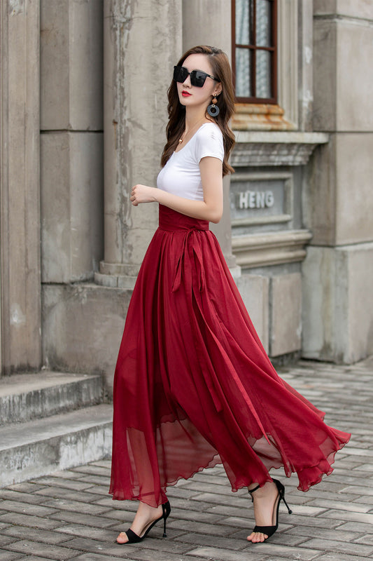 Woman in a white top and red skirt standing in front of a stone building.
