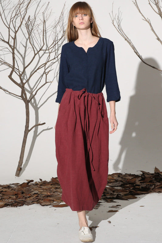 A woman wearing a navy top and a wine red maxi skirt with decorative buttons and two pockets on each side, standing outdoors.