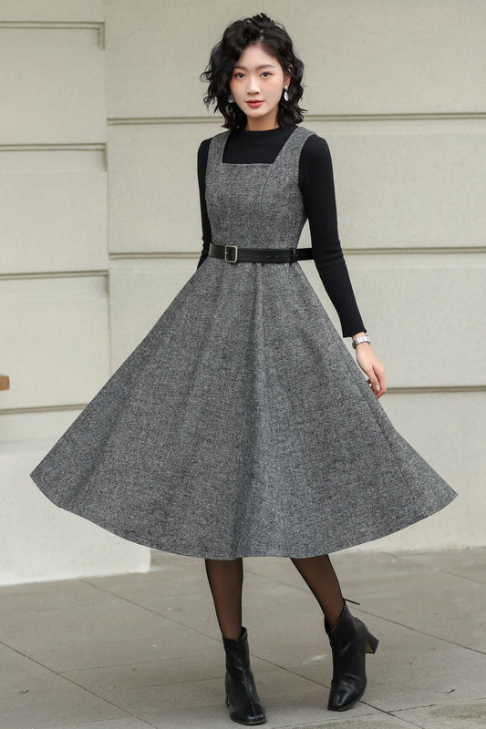 Woman wearing a gray dress over a black long-sleeve shirt against a light-colored wall.