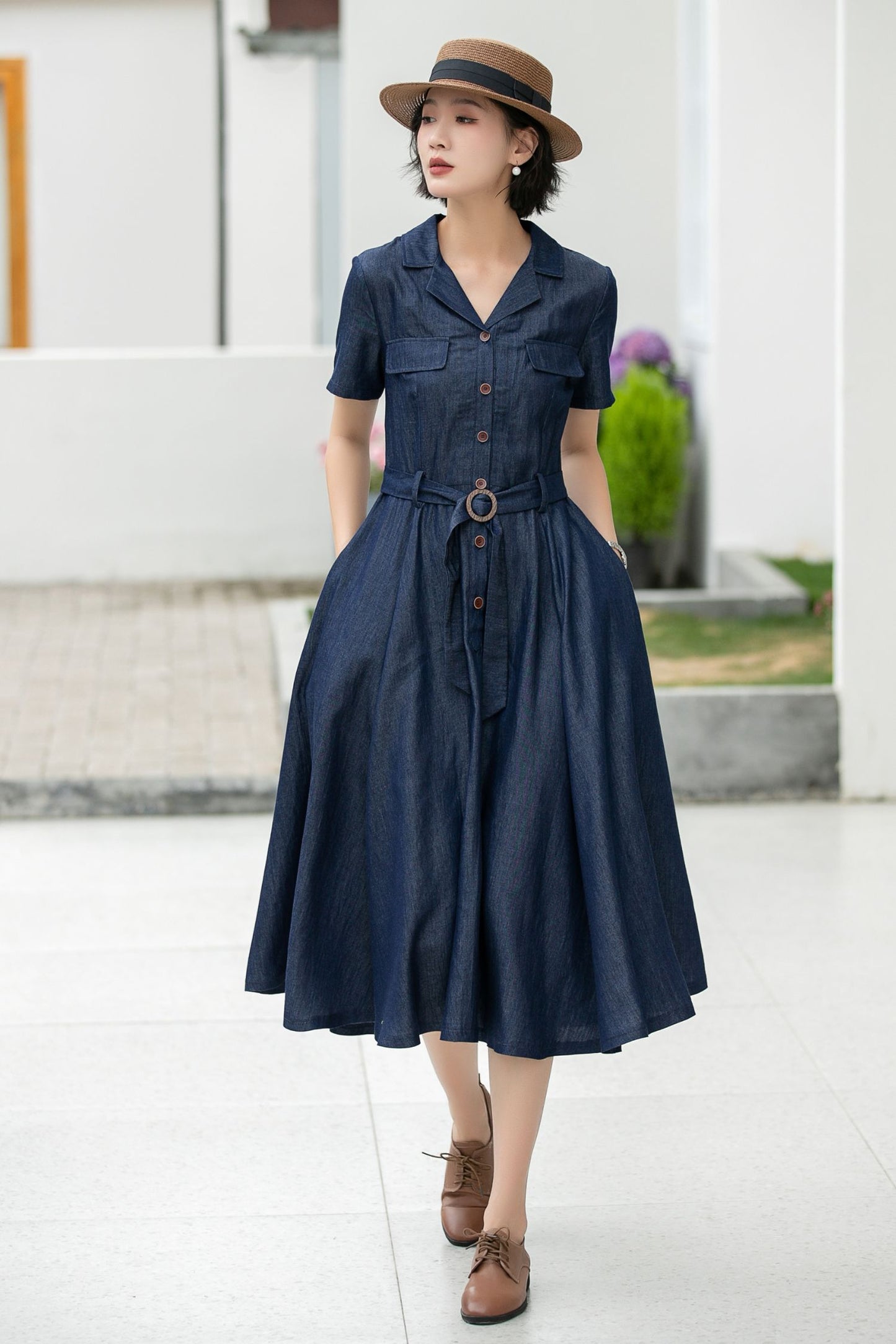 Woman wearing a navy dress with a belt and brown shoes, standing outdoors.