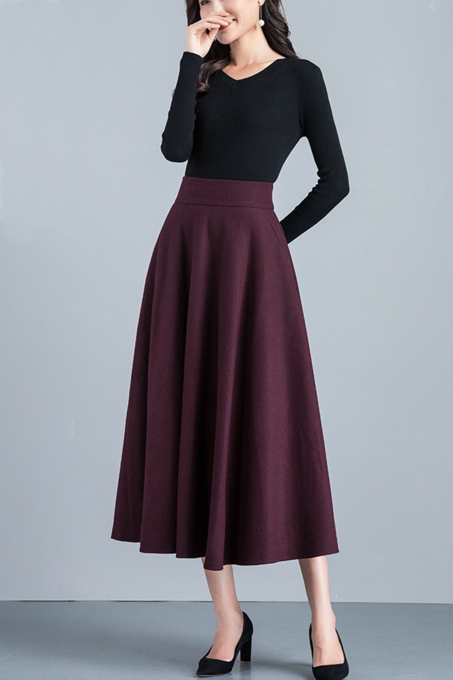Woman wearing a black top and burgundy skirt on a gray background