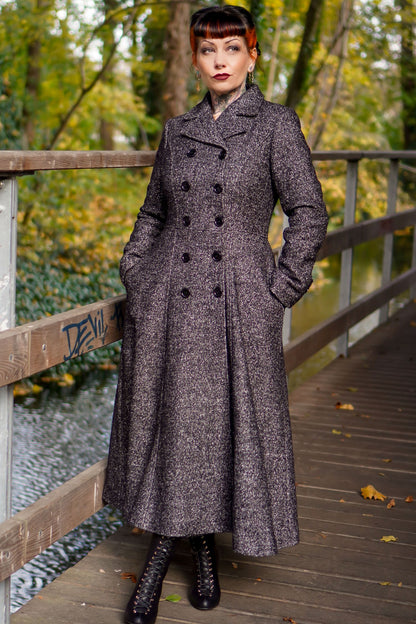 A woman standing on a bridge wearing a long gray double-breasted wool maxi coat with notched collar and two pockets, paired with black boots.