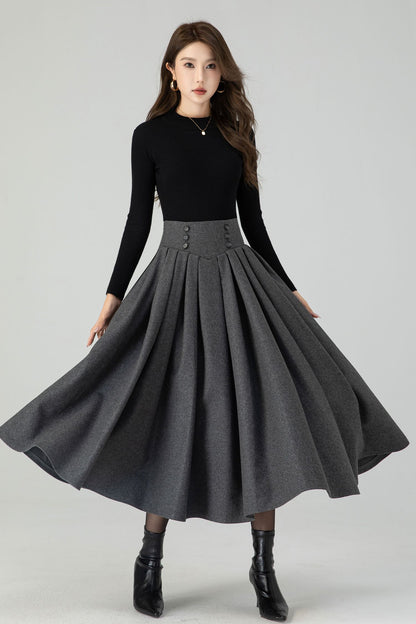 A model wearing a long pleated midi skirt in a deep gray color, paired with a black long-sleeve top and black ankle boots.