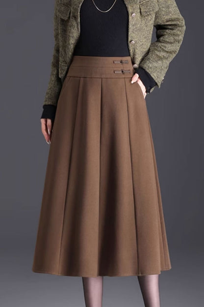 A line midi wool winter skirt in brown, with side pockets and a side zipper closure. The model is wearing a black jacket and a black top, standing against a grey background.