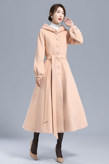 A stylish woman wearing a beige long wool coat with hood, lantern sleeves, and a single-breasted design, paired with dark shoes.