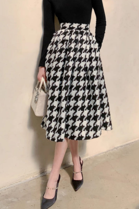 Person wearing a black and white houndstooth patterned skirt with a plain background