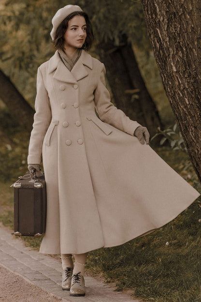A woman in a long beige wool coat with double-breasted construction, button front closure, and pleating details, walking outdoors.