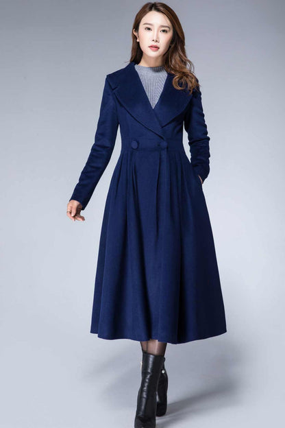 A woman standing wearing a navy blue wool princess coat with long sleeves, a lapel collar, and pleated waist detail.