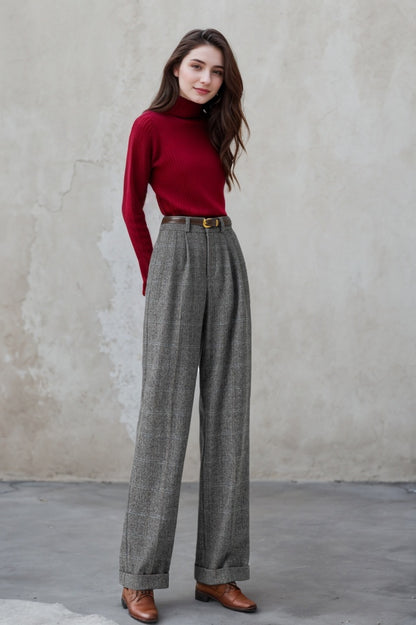 A woman standing against a plain background, wearing wide leg winter long wool pants with a checkered pattern, in a gray color, paired with a red turtleneck top.