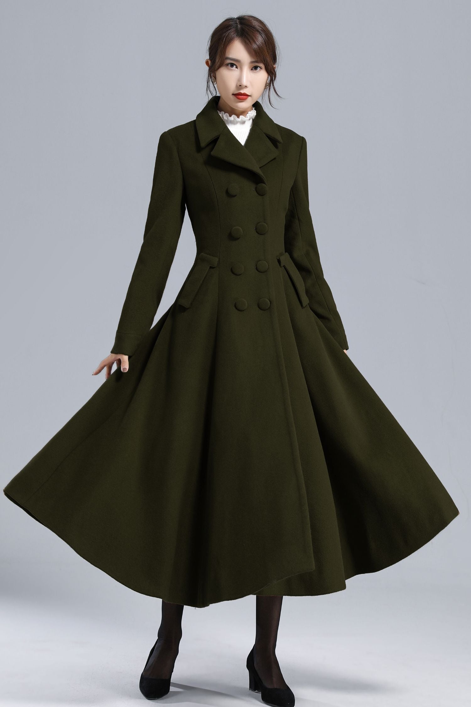 Woman wearing a long dark green coat on a gray background