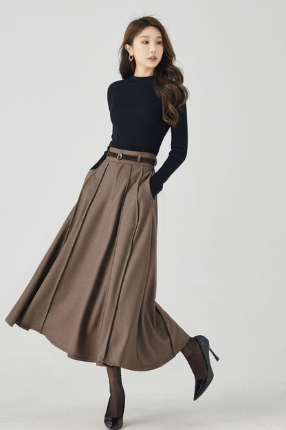 A woman modeling a brown pleated high-waisted wool midi skirt with a black top and accessories.