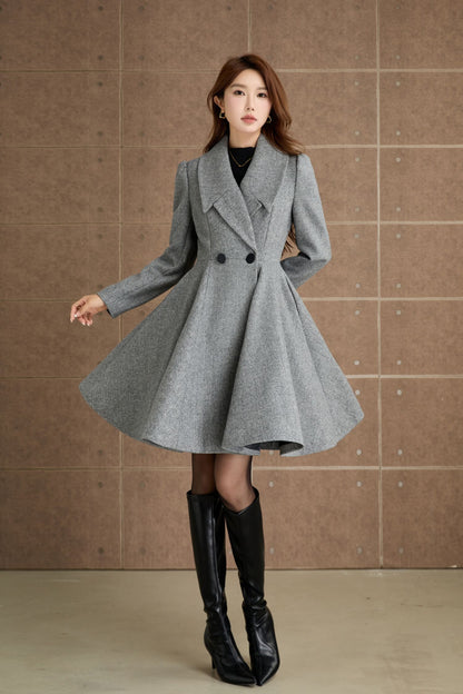 A woman modeling a fit and flare gray wool coat with a lapel collar and front button closure, paired with black boots.