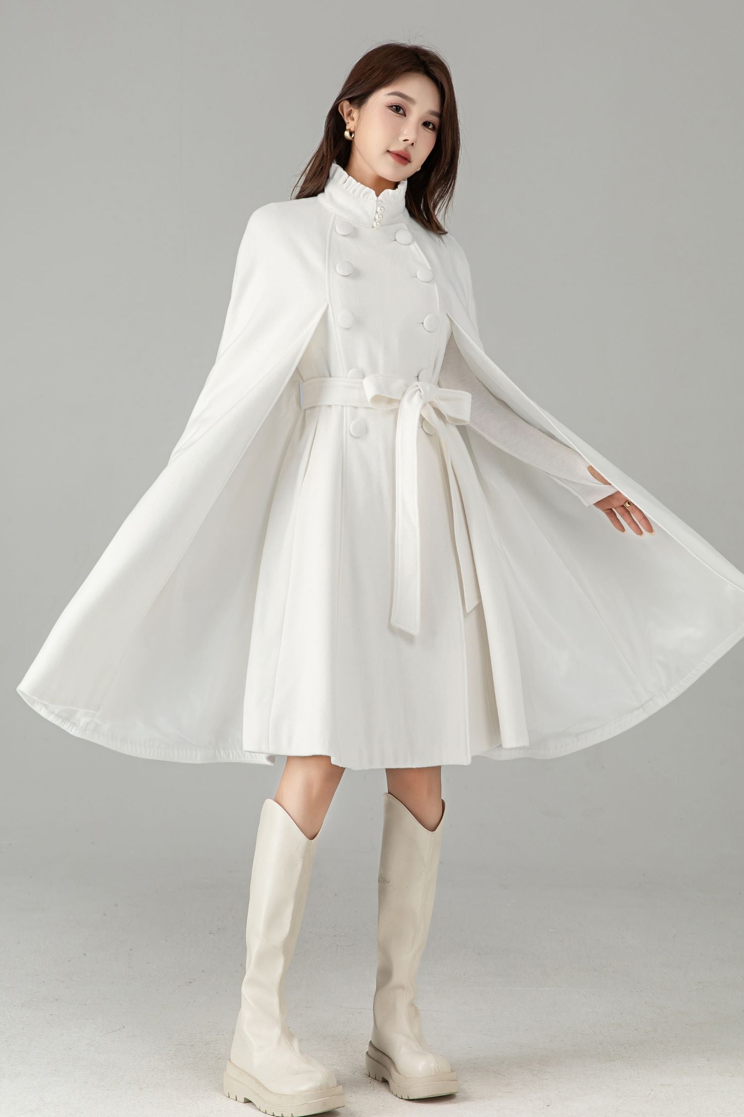 Woman wearing a white dress with long sleeves and a belt, standing against a plain background.