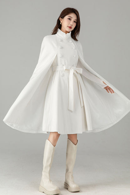 Woman wearing a white dress with long sleeves and a belt, standing against a plain background.