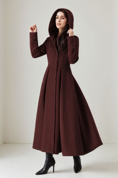 A woman wearing a long brown wool coat with a hood, posing against a plain background.