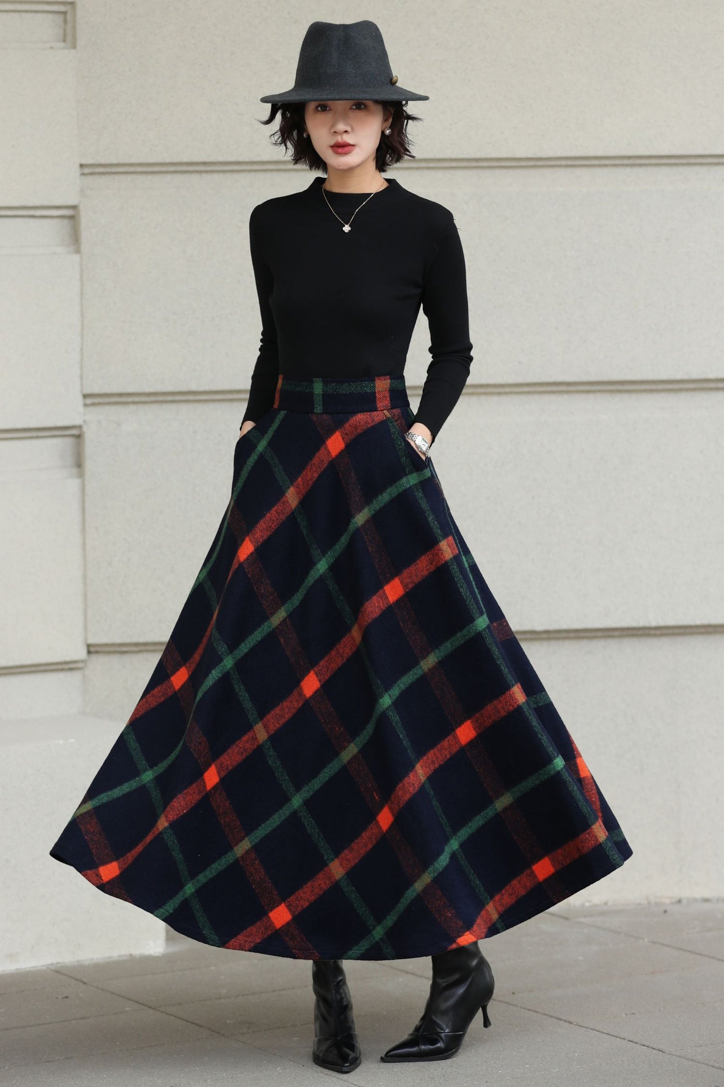 Person wearing a black top and plaid skirt with a hat against a light-colored wall.