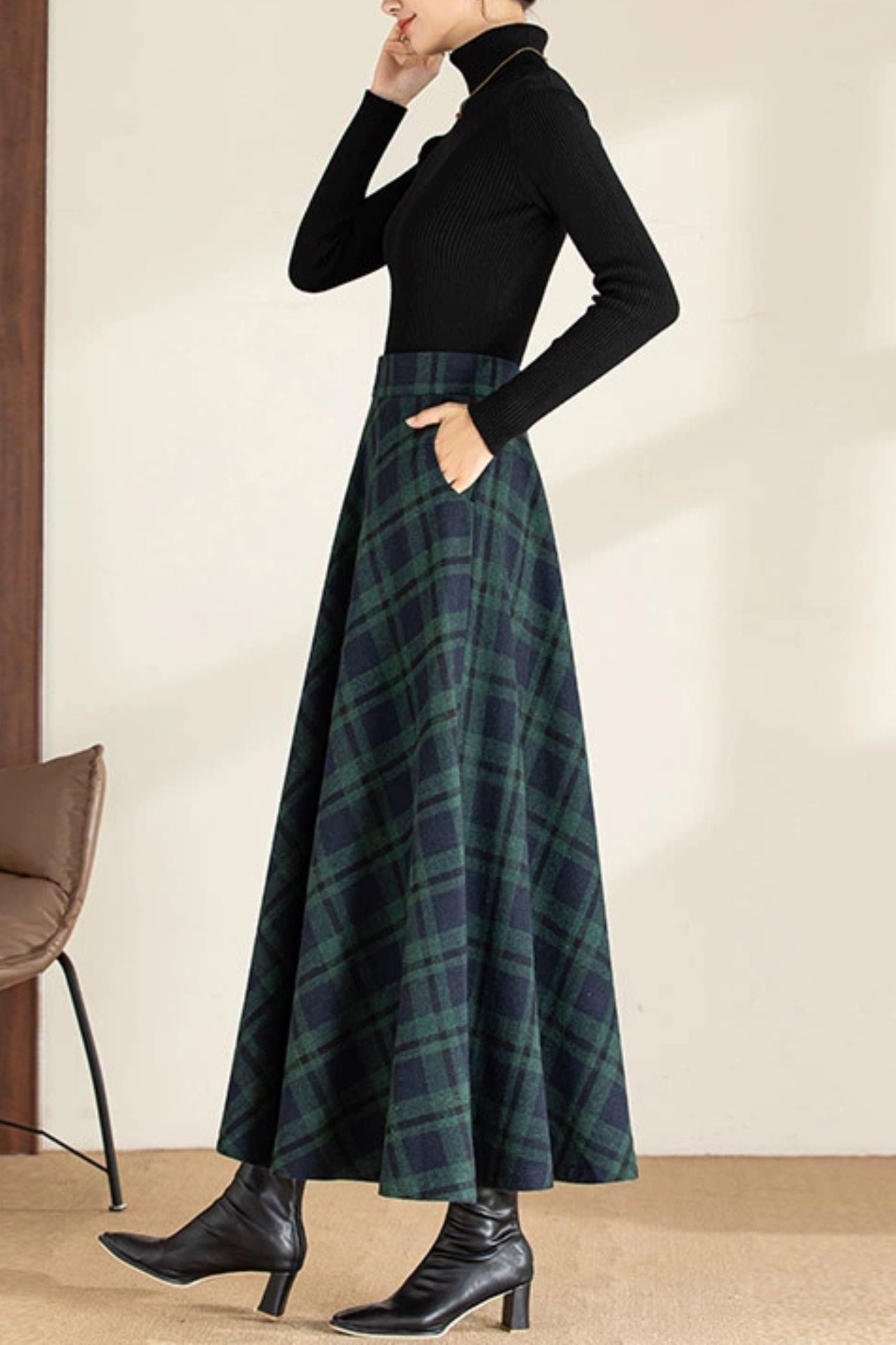 Person wearing a black turtleneck and plaid skirt with black boots indoors.