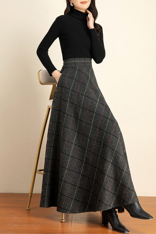 Person wearing a black turtleneck and plaid skirt on a wooden floor with a beige wall background