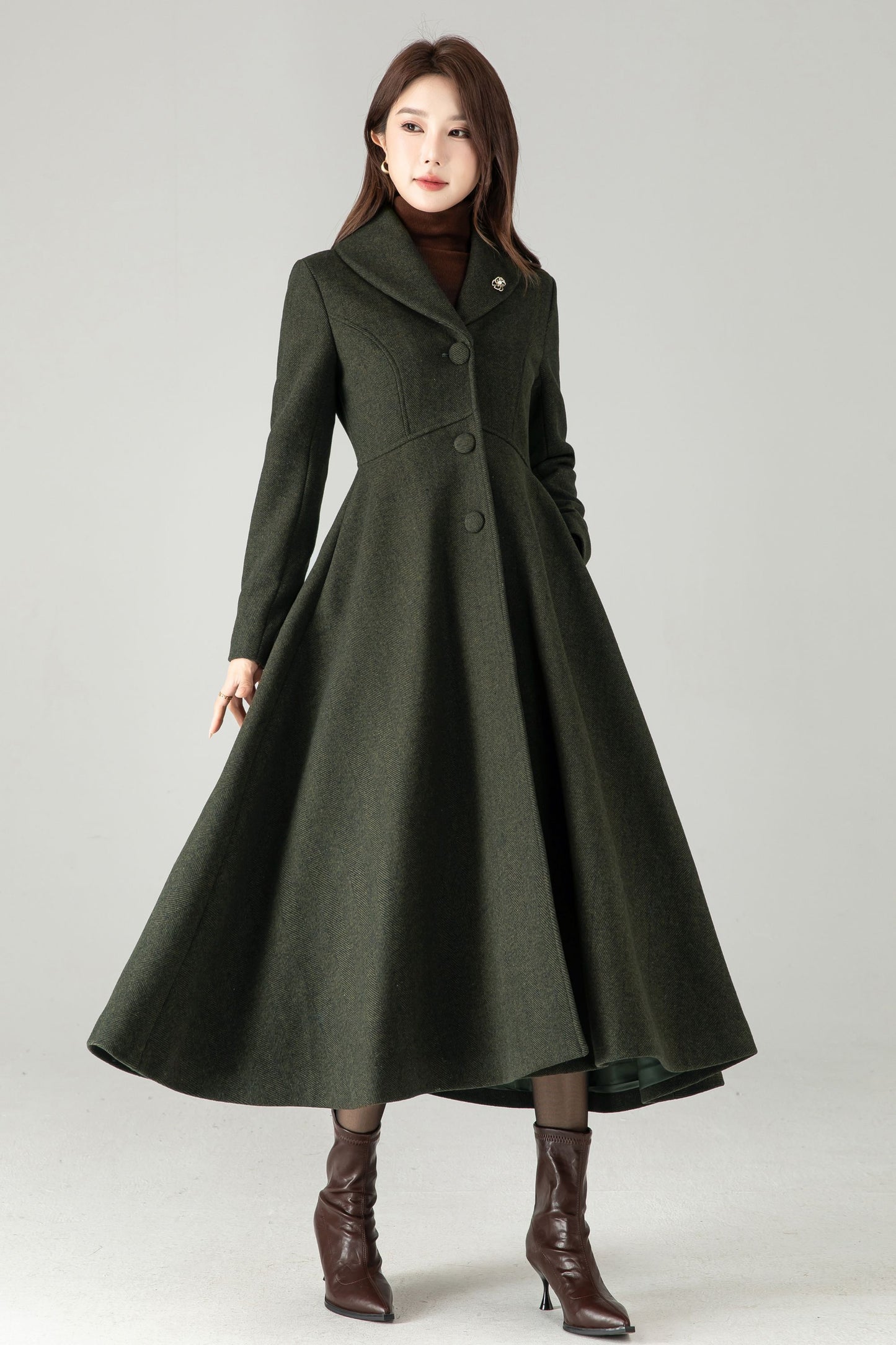 Woman wearing a long dark green coat on a gray background
