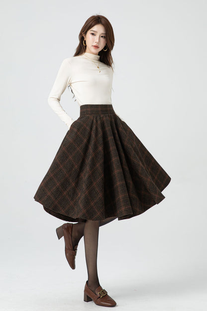 A knee-length pleated plaid winter wool skirt in a brown and white color scheme, worn by a female model with a white top and dark shoes.