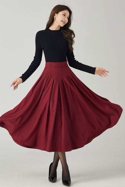 A woman in a burgundy wool pleated midi skirt with a black top, posing with one hand raised to her hip.