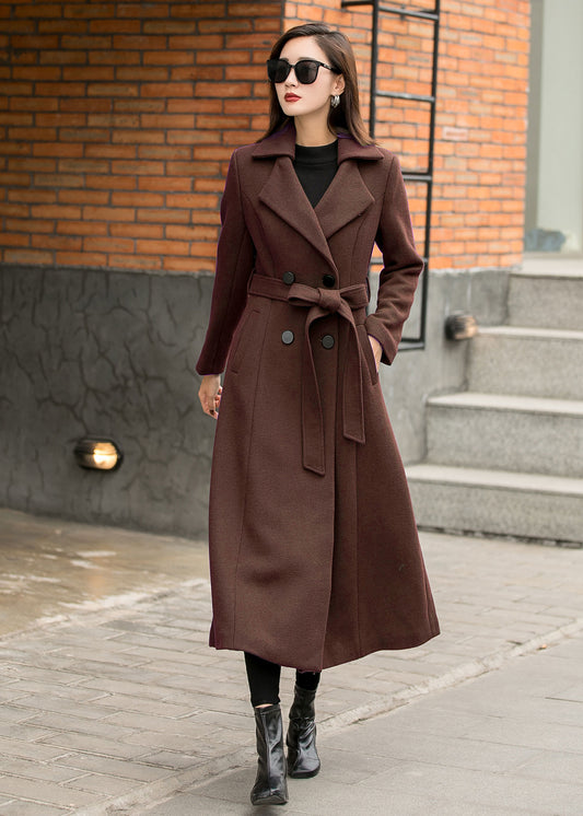 Woman wearing a brown coat standing on a street with a brick wall background