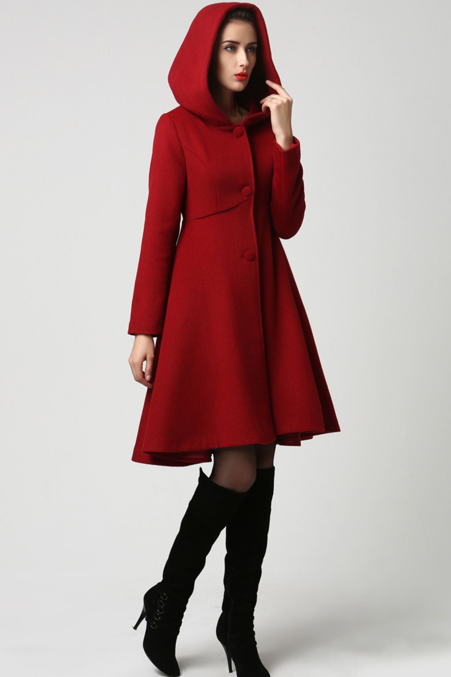 A model wearing a handmade flared red wool coat with a hood, featuring a structured bodice and long sleeves with button closure.
