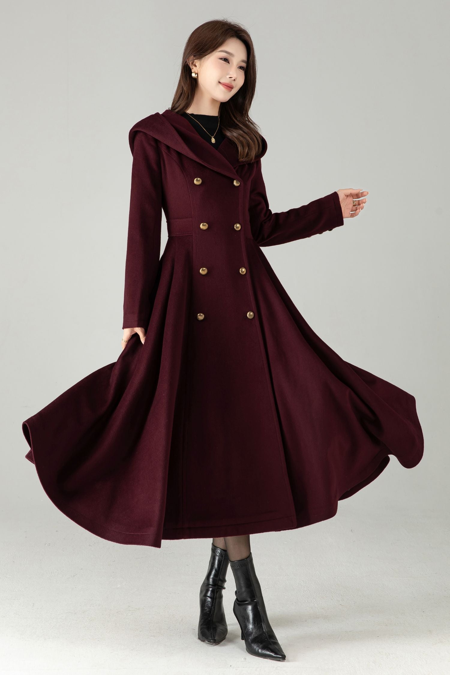 Woman wearing a burgundy coat with gold buttons on a gray background