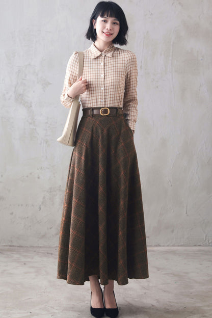 A woman wearing a high-waisted, vintage plaid wool long skirt with a belt and a checkered pattern. She is also wearing a button-up shirt and a bag is visible in her hand.