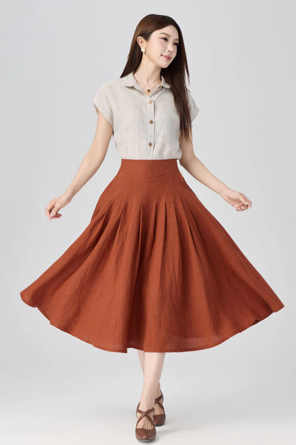 May include: A short-sleeved, beige and white pinstriped button-down shirt with a collar paired with a high-waisted, rust-colored midi skirt featuring deep box pleats that create a full, flared silhouette and a smooth, fitted waistband.
