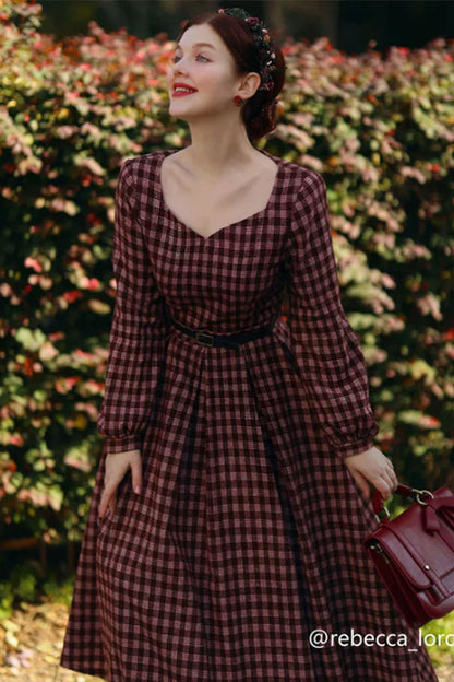 A woman wearing a long sleeve, plaid wool dress with a fit and flare silhouette, in an outdoor setting.