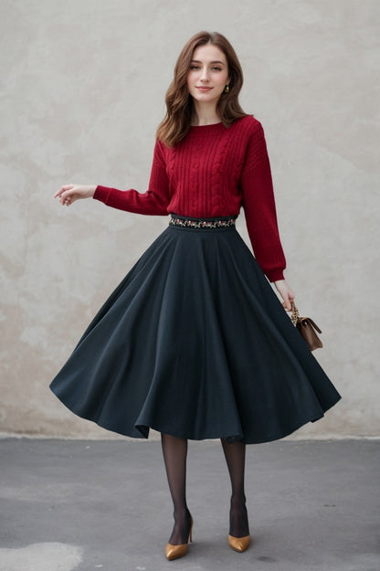 A woman wearing a black A-line midi wool skirt with an embroidered design at the waist, paired with a red sweater and black heels. The skirt has a vintage circle design.