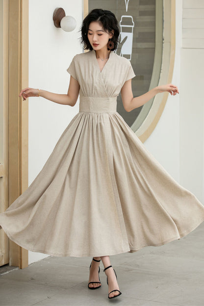 Woman wearing a beige dress standing in a room with a mirror.