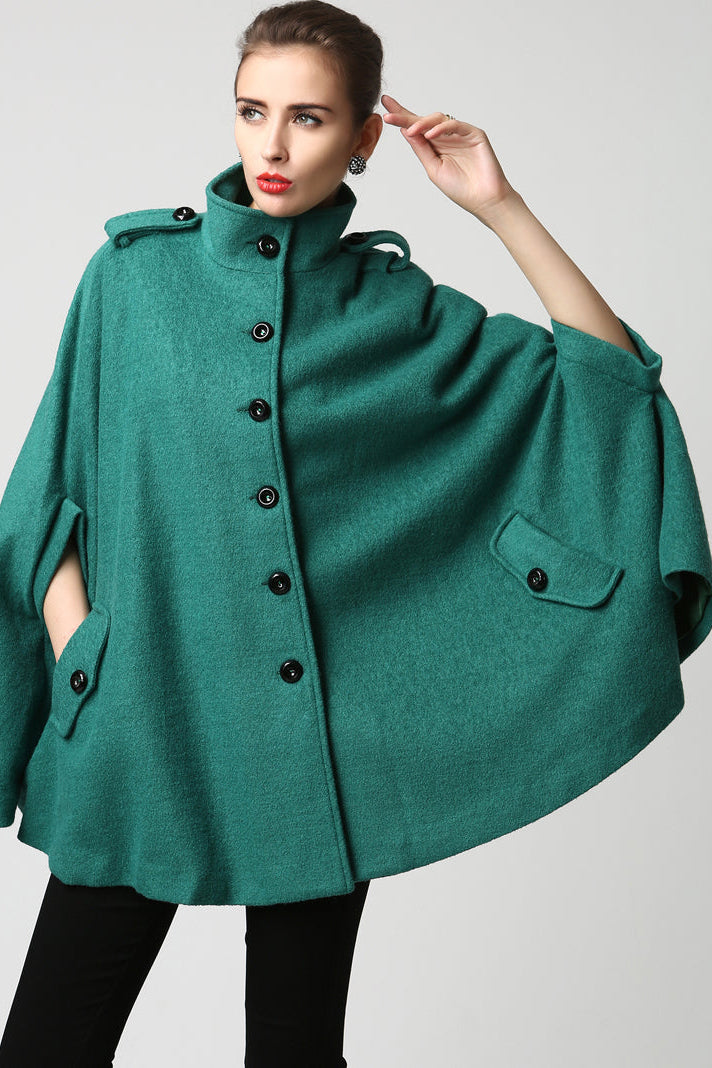 Woman wearing a green poncho with black buttons on a light gray background