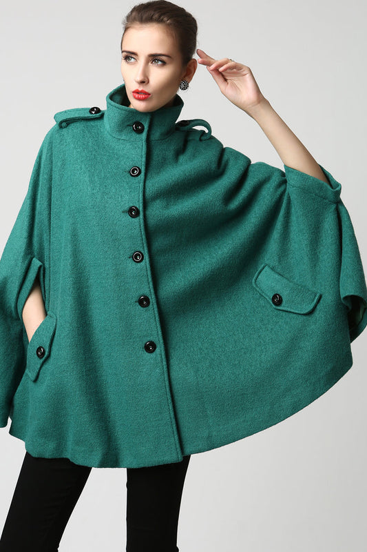 Woman wearing a green poncho with black buttons on a light gray background