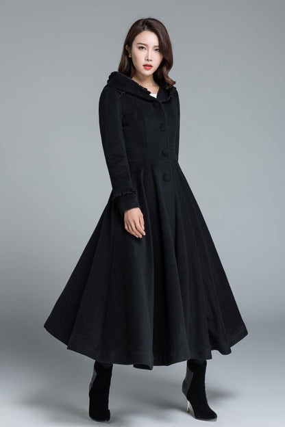 A woman wearing a black wool winter princess coat with a hood, long sleeves, and a regular fit. The coat has a ruffle detail on the shoulder and hood.