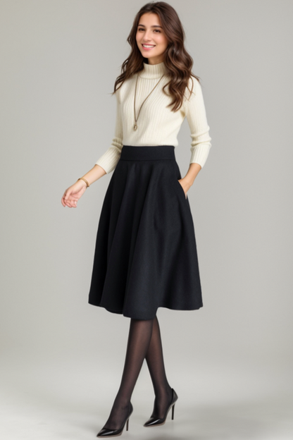 Woman wearing a cream sweater, black skirt, and black shoes on a gray background