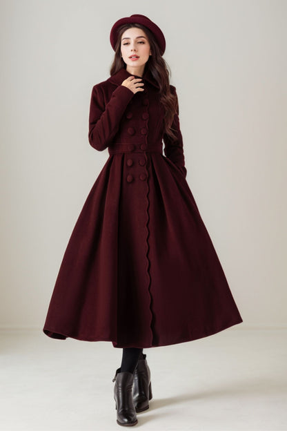 A woman wearing a burgundy long coat with pleated front, cinched waist, and full skirt, paired with a black hat and black boots.