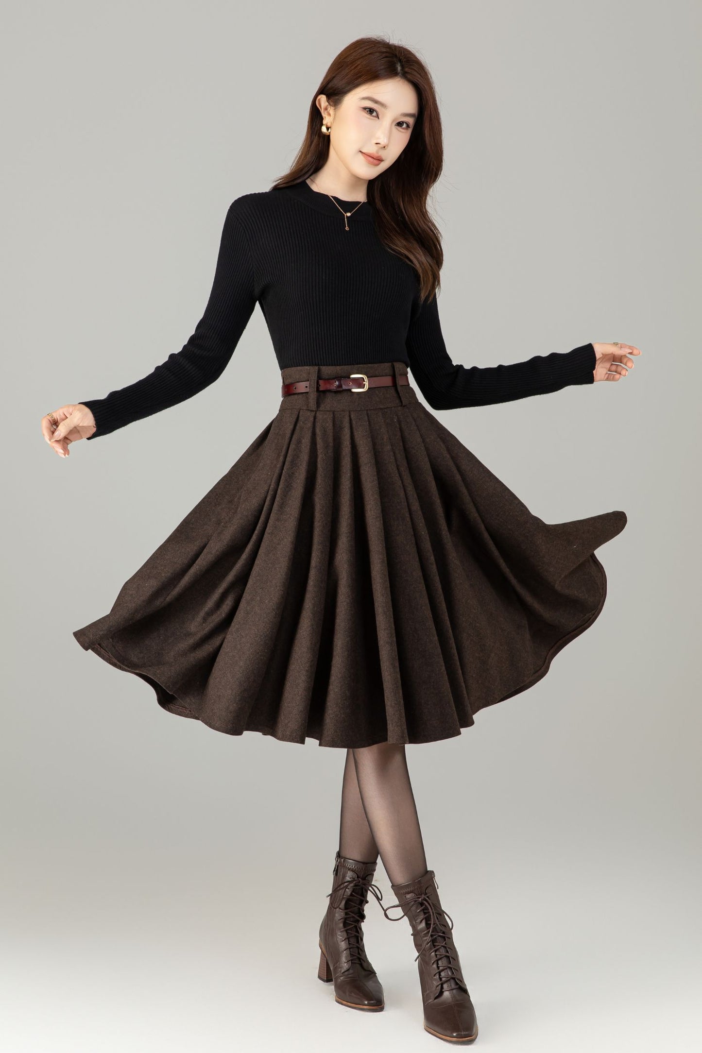 Woman wearing a black top and brown skirt with a belt on a gray background