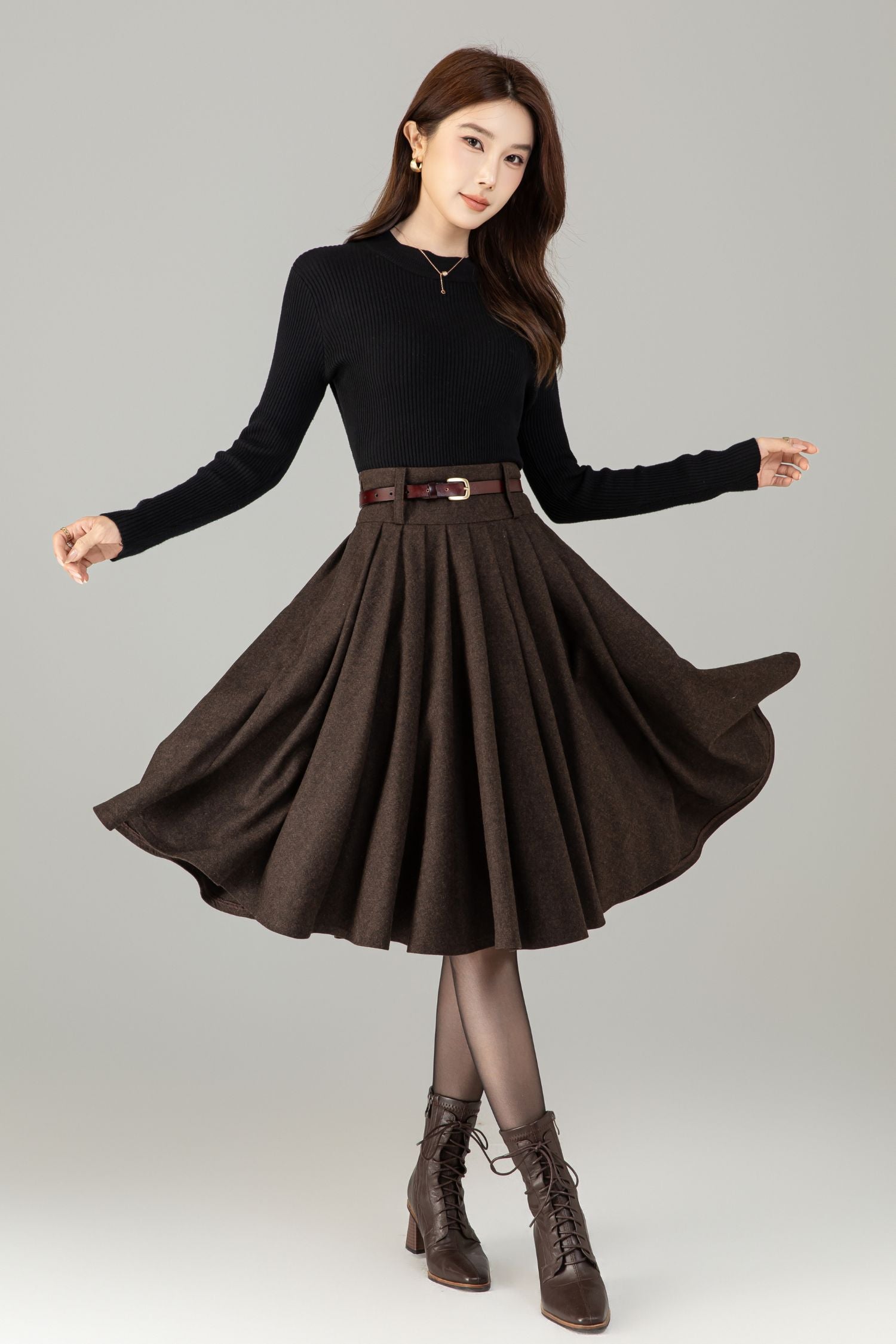 Woman wearing a black top and brown skirt with a belt on a gray background