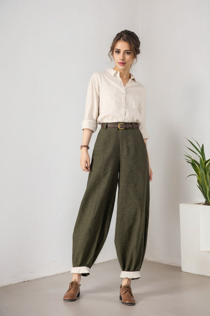 Woman wearing a white shirt and green pants standing against a plain background