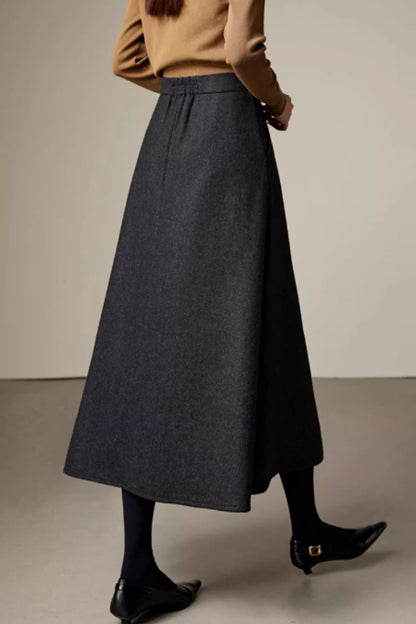 Person wearing a long dark gray skirt with a neutral background