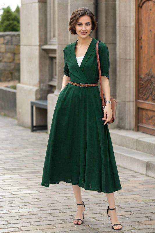 May include: A dark green dress with a V-neckline and short sleeves. The dress features a brown belt cinching the waist and a flowing skirt. The model is wearing black heels and carrying a brown purse. The dress is suitable for a variety of occasions.