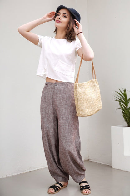 Woman wearing a white top, gray wide-leg pants, and black sandals, holding a beige bag against a white background.