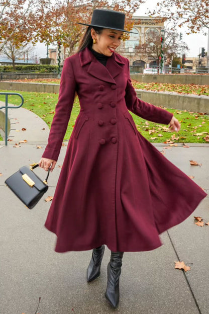 Woman in a burgundy coat and black hat walking outdoors on a sidewalk.