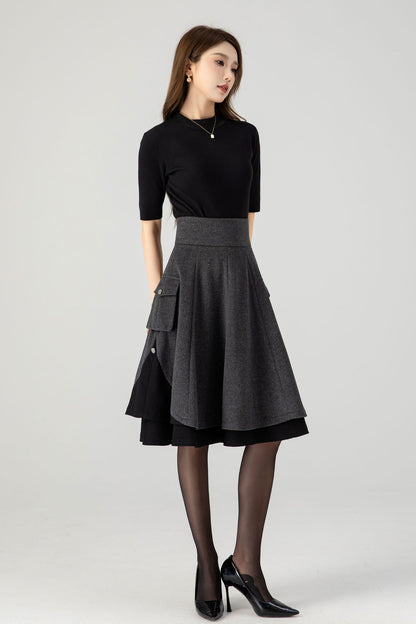 A woman standing wearing a vintage green wool skirt with a high-rise, fit and flare silhouette, featuring two side pockets and a back zipper closure, above knee length.