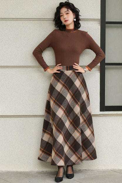 Woman wearing a brown top and plaid skirt against a light-colored wall.