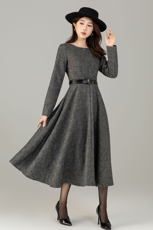 Woman wearing a gray dress with a black belt and black hat on a gray background