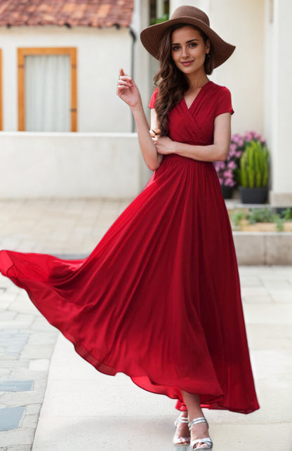 A woman in a flowing red chiffon empire waist wedding dress with cap sleeves, a V-neckline, and a maxi length that reaches the calf. She is wearing a wide brim hat and her dress is flowing in the wind.